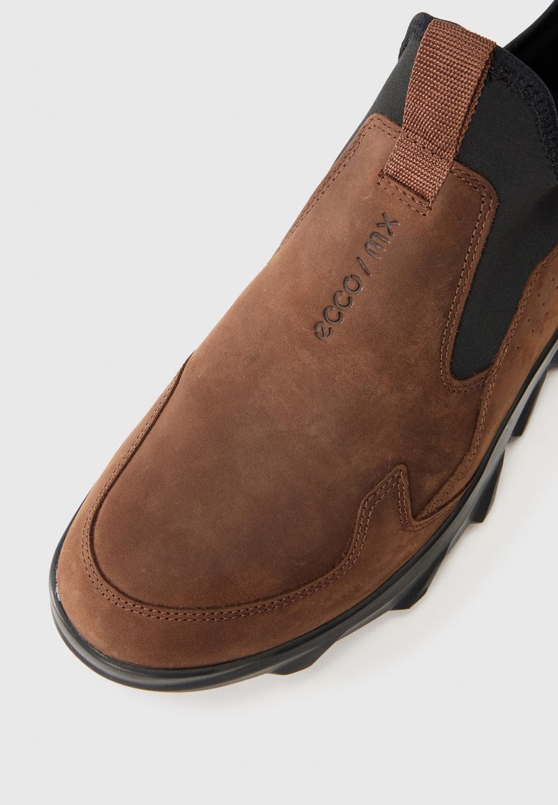 Braunes Wildleder-Slipper mit einem strukturierten schwarzen elastischen Einsatz, genähten Details und Gummisohle. Das Logo an der Seite lautet "ecco / mx."