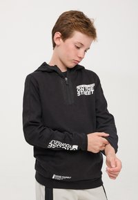 Felpa nera con cappuccio e collo con zip, testo stampato bianco sul petto e sulle maniche, tessuto morbido e vestibilità comoda.