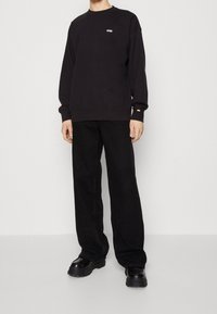Felpa nera con collo tondo e piccolo logo bianco. Abbinata a pantaloni neri a gamba larga e scarpe nere chunky. Look casual, tessuto testurizzato.