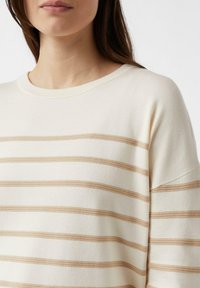Kremowy sweter z poziomymi beżowymi paskami, z okrągłym dekoltem i miękką fakturą. Lekko szerokie rękawy i luźny krój.