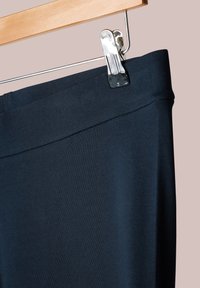 Leggings de color azul marino hechos de una tela elástica, con una cinturilla suave, colgando de un perchero de madera con un clip de metal.