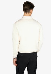 Sudadera blanca con puños y dobladillo acanalados, combinada con pantalones cargo negros, mostrando la vista trasera. Textura suave, diseño simple, sin logotipos visibles.