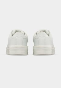 Ζευγάρι λευκών πάνινα παπούτσια χαμηλού τύπου, εμφανιζόμενα από πίσω, με ανάγλυφο λογότυπο εταιρείας στην ταμπέλα της φτέρνας και παχιά λαστιχένια σόλα.