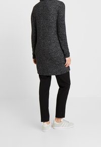 Graues meliertes Langarm-Tunikakleid in knielanger Ausführung, kombiniert mit schwarzen Hosen und hellgrauen Sneakers. Schlichtes Design mit weichem Textil.