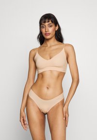 Set od braleta i tangica bez krojeva ima glatku teksturu, minimalni dizajn i tanke naramenice. Bralet ima V-izrez, a tangice nizak pojas.
