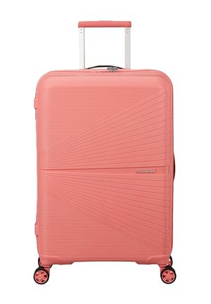 Grande valigia rigida color corallo rosa con linee diagonali testurizzate, manico retrattile e quattro ruote girevoli.