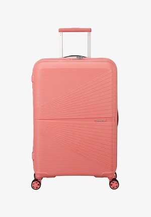 Grande valigia rigida color corallo rosa con linee diagonali testurizzate, manico retrattile e quattro ruote girevoli.