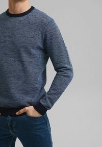 Granatowy sweter o fakturowanej powierzchni z okrągłym dekoltem i ściągaczami. Posiada pleciony wzór dla dodatkowego wykończenia. W zestawie z niebieskimi dżinsami.