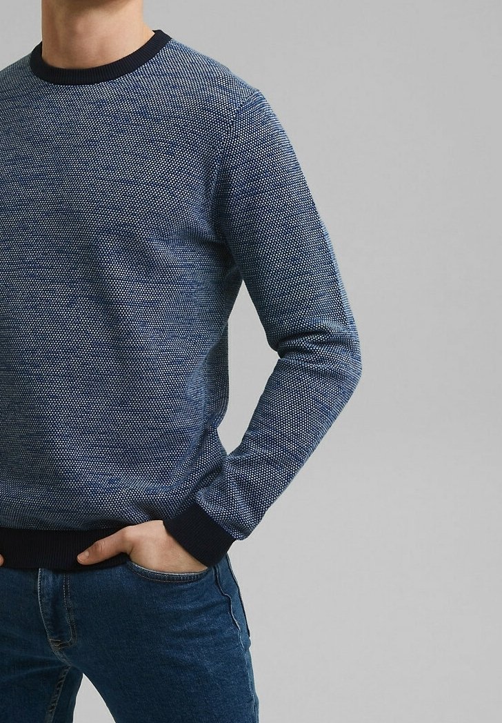Granatowy sweter o fakturowanej powierzchni z okrągłym dekoltem i ściągaczami. Posiada pleciony wzór dla dodatkowego wykończenia. W zestawie z niebieskimi dżinsami.