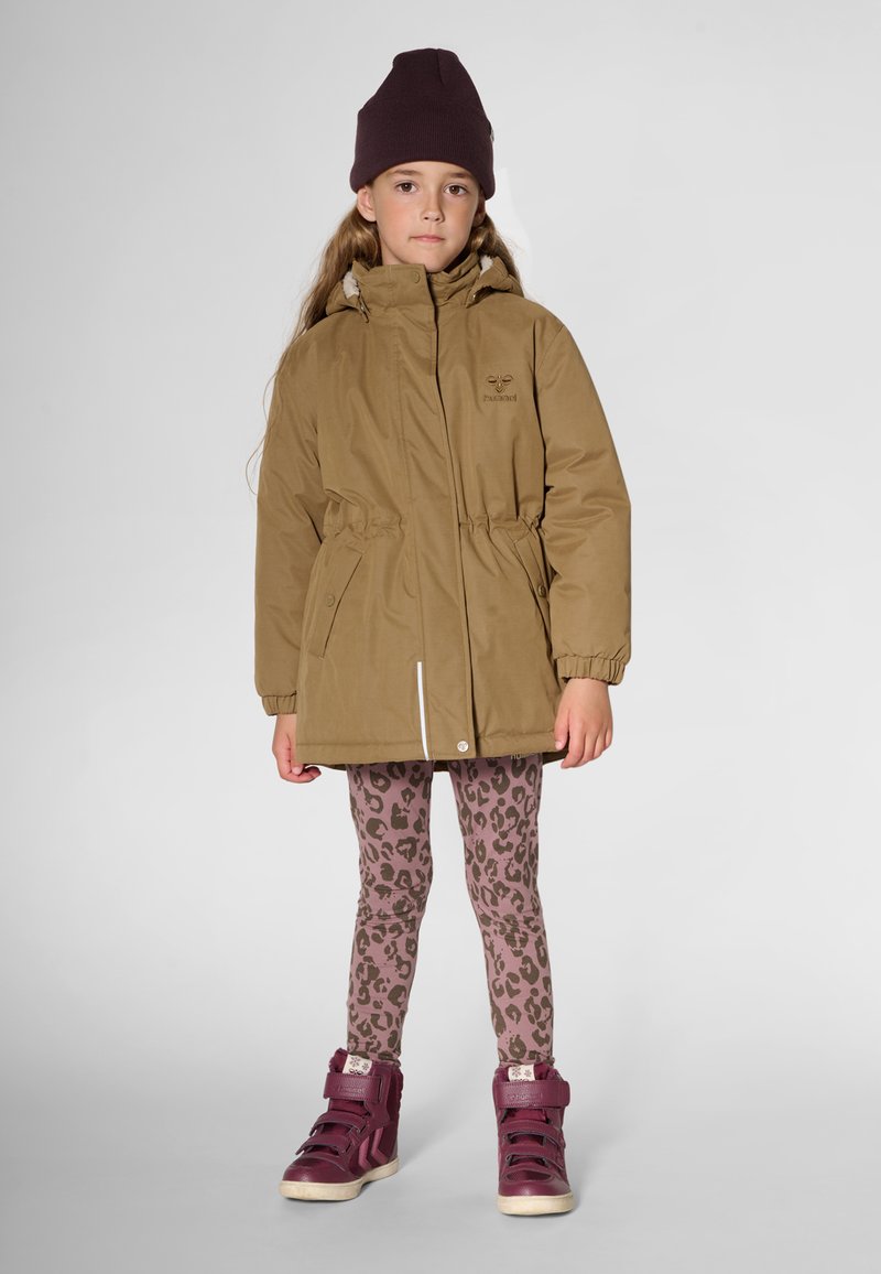 Veste parka kaki avec taille élastique, poches frontales et col montant ; associée à des leggings imprimé léopard rose et des baskets montantes bordeaux.