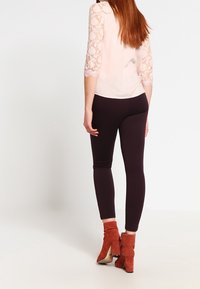 Světle růžová blůza s krajkovými rukávy, kombinovaná s tmavými legínami a oranžovými kotníkovými botami. Blůza má kulatý výstřih a přiléhavý střih.