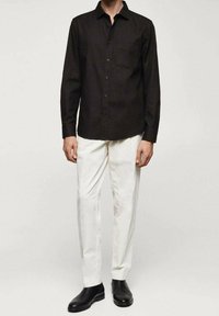 Czarna koszula z długim rękawem i zapięciem na guziki, w połączeniu z białymi spodniami i czarnymi botkami za kostkę. Subtelny detal kieszeniowy na koszuli.
