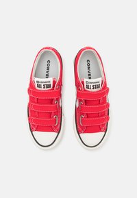Zapatillas de lona rojas con cordones elásticos y suelas de goma. Presentan una puntera blanca, detalles en negro y el logo "Converse All Star" en la lengüeta.