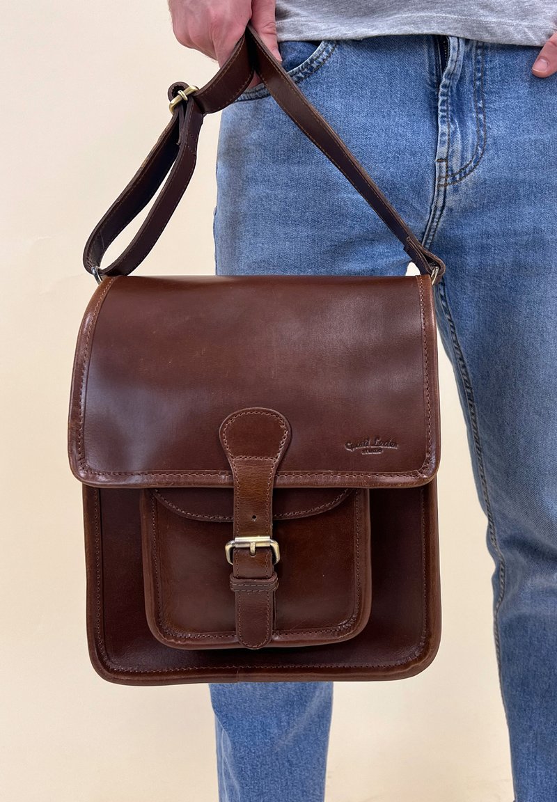 Brown leather messenger bag with a front flap, buckle closure, and an exterior pocket. Smooth texture and adjustable shoulder strap.