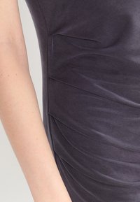 Ciemnoszara sukienka o zmarszczonej teksturze, wykonana z miękkiego materiału, o dopasowanym kroju oraz subtelnych plisach po bokach, które dodają wizualnego zainteresowania.