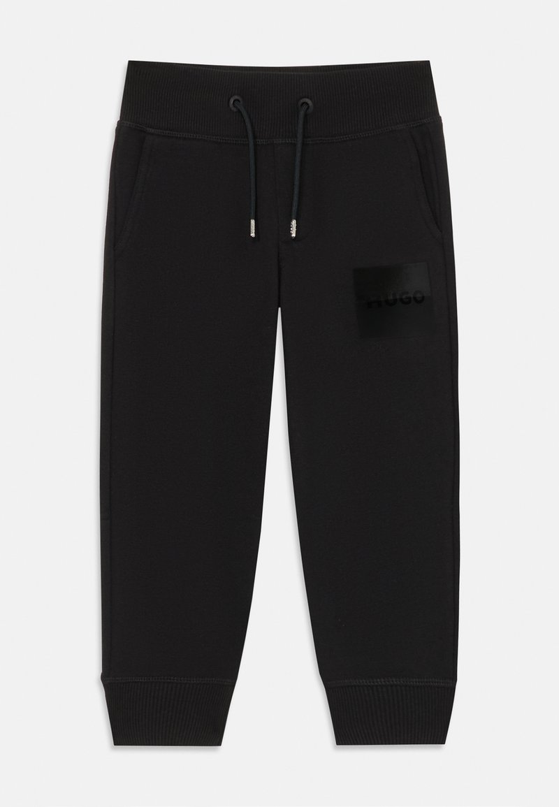 Melnas sporta bikses, izgatavotas no mīksta auduma, ar elastīgu jostasvietu, aukliņu un melnu logotipa uzlīmi kreisajā augšstilbā.