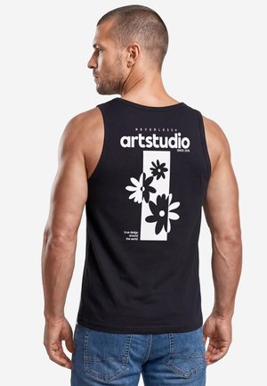 Man wearing black sleeveless shirt with white floral art and "artstudio" text on the back, paired with blue denim jeans.