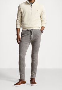 Sudadera de cremallera de cuarto en color crema claro; pantalones de punto texturizado grises con cordón; zapatillas de cuero marrón; ajuste casual.
