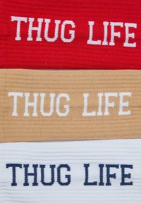 Tre tygremsor, färgade röd, beige och vit, var och en broderad med "THUG LIFE" i kontrasterande färger, med ett strukturerat mönster.