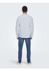 Camicia a maniche lunghe a righe azzurro chiaro con orlo curvo e polsini con bottoni, abbinata a jeans blu scuro e scarpe da ginnastica chiare.