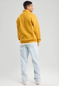 Yellow fleece pullover with a high collar, paired with light blue baggy jeans. Standard fit with minimal detailing and a smooth texture.