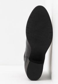 Czarna skórzana podeszwa buta z teksturowanym wzorem i zaokrąglonym kształtem, z rowkami zapewniającymi przyczepność. Rozmiar oznaczony jako 37.