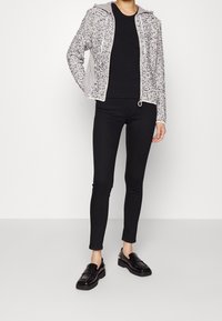 Grå och svart mönstrad zip-up hoodie med huva, bärs över en svart tröja, kombinerad med svarta skinny jeans och svarta loafers.