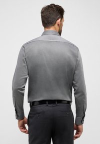 Grau gemustertes Langarmhemd mit Button-Down-Kragen, kombiniert mit dunkelgrauen Hosen und einem schwarzen Gürtel. Enthält Knopf-Akzente an den Manschetten.