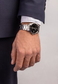 Edelstahlarmbanduhr mit einem silbernen Armband und einem schwarzen Zifferblatt, ausgestattet mit weißen Stundenmarkierungen, Datumsanzeige und rundem Gehäuse.