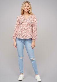 Blusa a stampa floreale in rosa pastello con dettagli arricciati, abbinata a jeans skinny sbiaditi blu chiaro e sneakers bianche.