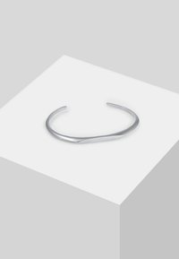Bracciale in metallo argento con design intrecciato, caratterizzato da una superficie liscia e lucida e estremità aperte per la regolabilità.