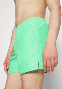 Zöld fürdőnadrág rugalmas derékkal és oldalsó nyílásokkal, könnyű anyagból készült, a szegélyén egy kis fehér Nike logóval.