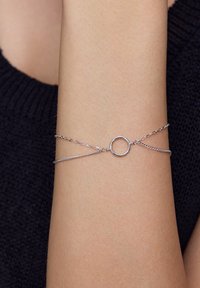 Srebrna bransoletka z dwiema delikatnymi łańcuszkami i okrąłym charms, charakteryzująca się gładką, refleksyjną powierzchnią oraz prostym, minimalistycznym wzornictwem.