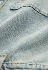 Tessuto di denim azzurro chiaro, con una texture liscia e un motivo di tessitura visibile. Presenta dettagli di cucitura lungo i bordi e nell'area delle tasche.