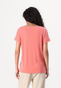 T-shirt corallo a maniche corte con vestibilità rilassata, scollatura rotonda e risvolti. Tessuto morbido con una texture liscia, design leggero.