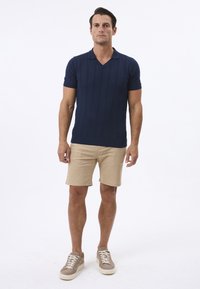 Marineblaues Kurzarm-Polo mit strukturiertem Muster und V-Ausschnitt; kombiniert mit beigen Shorts und beige-farbenen Sneakers. Einfaches, lässiges Design.