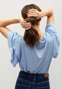 Lyseblå kortærmet skjorte lavet af blødt stof, med løs pasform og draperet design. Båret med højtaljede mørke denim jeans.