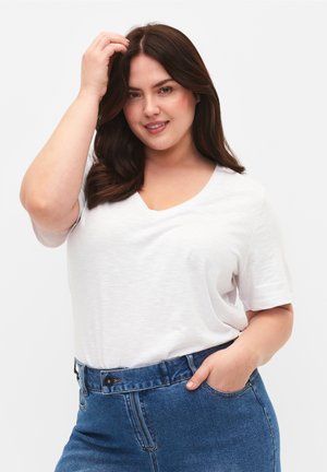 Camiseta blanca de cuello en V, hecha de una tela ligera, de manga corta, combinada con unos vaqueros de mezclilla azul de cintura alta.