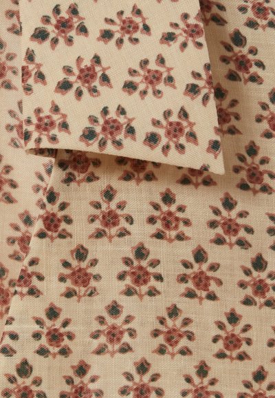 Tessuto a fantasia floreale con sfondo beige, caratterizzato da fiori rossi e verdi in un motivo ripetuto e una superficie testurizzata.
