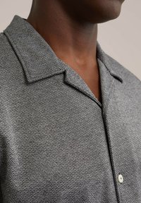 Camisa de patrón espiga en gris y blanco con cuello, que presenta un cierre de un solo botón y una tela texturizada.