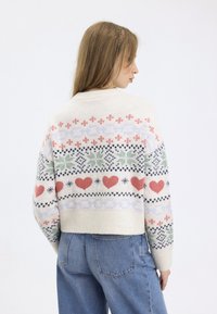 Cream-colored knit sweater featuring multicolored patterns of hearts, snowflakes, and floral designs. Ribbed cuffs and hem. Cropped fit.