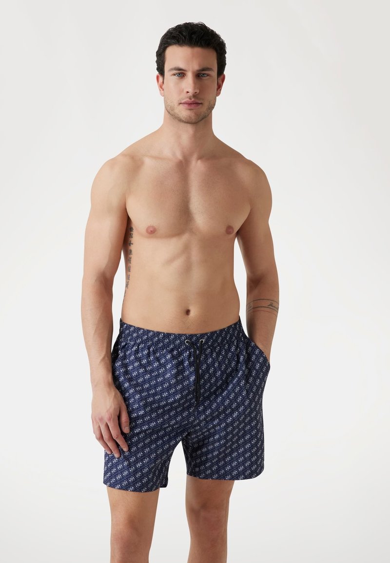 Pantaloni da bagno blu a motivo con una cintura elasticizzata, tasche laterali e un cordoncino. Presenta un motivo ripetuto in toni di blu più chiari.