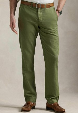 Grüne Baumwollhose mit Fronttaschen, geradem Schnitt und einem braunen Ledergürtel. Getragen mit braunen Schuhen, die ein lässiges Design präsentieren.