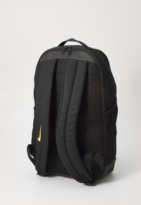 Μαύρο σακίδιο πλάτης με επενδεδυμένες ιμάντες, μπροστινό θησαυροφυλάκιο με φερμουάρ, πλέγματα πλευρικές τσέπες και ένα μικρό κίτρινο λογότυπο Nike στο πλάι. Υφασμάτινο υλικό με υφή.
