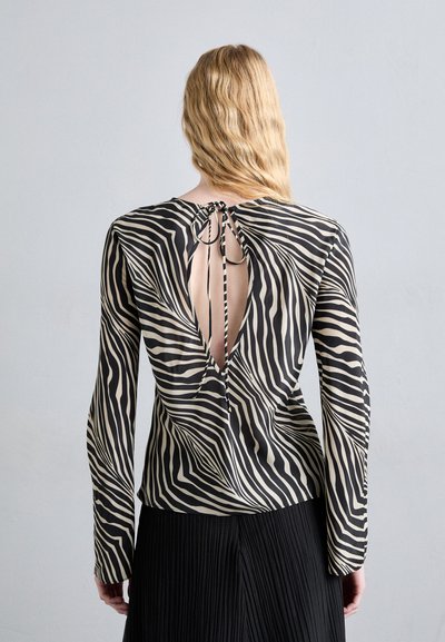 Long-sleeve blouse in black and beige zebra print, featuring an open back with a tie closure. Smooth fabric and fitted design.