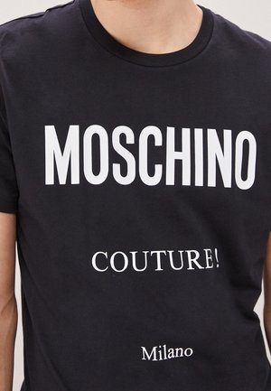 Czarny bawełniany t-shirt z dużym białym napisem: "MOSCHINO" na górze, "COUTURE!" na środku i "Milano" na dole. Krótkie rękawy, okrągły dekolt.
