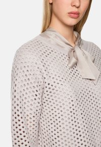Hellgrauer Strickpullover mit einem offenen Gewebe-Muster und einer seidigen Schleife am Ausschnitt, mit einem runden Kragen und strukturiertem Stoff.