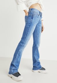 Jeans de ganga azul claro com um corte recto, cinco bolsos e um discreto rótulo da marca na parte de trás. Tecido texturizado com um acabamento suave.
