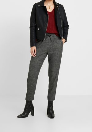Veste en cuir noire, pull en maille bordeaux, pantalon gris à carreaux, et bottines à talons noires. Mise en avant des matériaux et des textures.