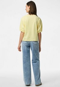 Gul topp med korta puffärmar, kombinerad med ljusblå vida jeans. Tyget verkar mjukt, med en enkel och ren design.